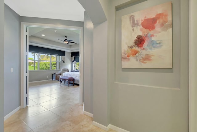 hall featuring light tile patterned flooring, a raised ceiling, and baseboards