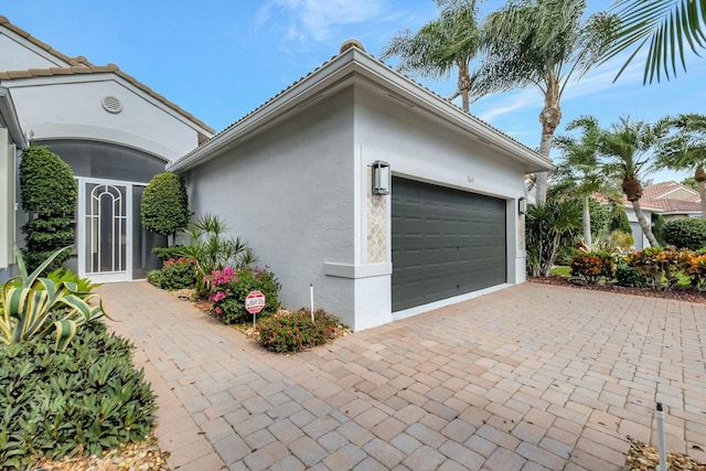 view of side of property featuring a garage, decorative driveway, and stucco siding