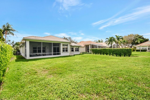 back of house with a sunroom, a tile roof, and a lawn