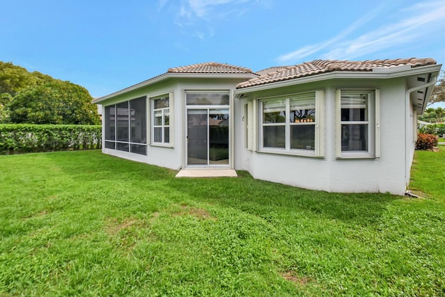 rear view of house featuring a sunroom, a tiled roof, stucco siding, and a yard