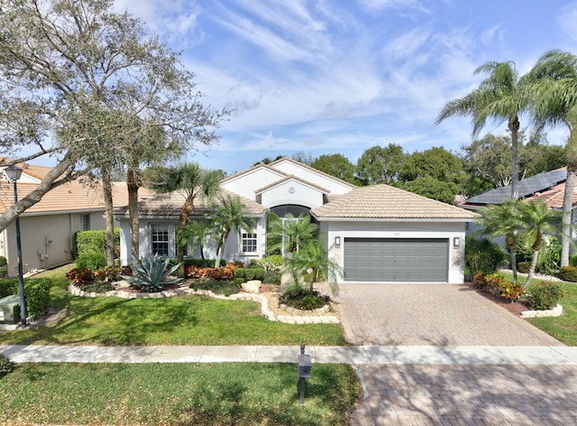 view of front facade with an attached garage, a tile roof, decorative driveway, stucco siding, and a front yard