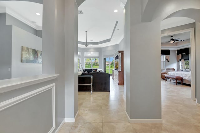 hallway featuring light tile patterned floors, visible vents, arched walkways, baseboards, and a tray ceiling