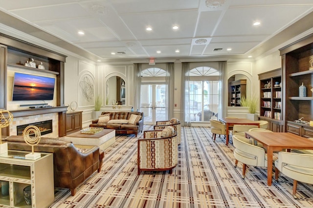 sitting room featuring built in shelves, a decorative wall, ornamental molding, a glass covered fireplace, and coffered ceiling