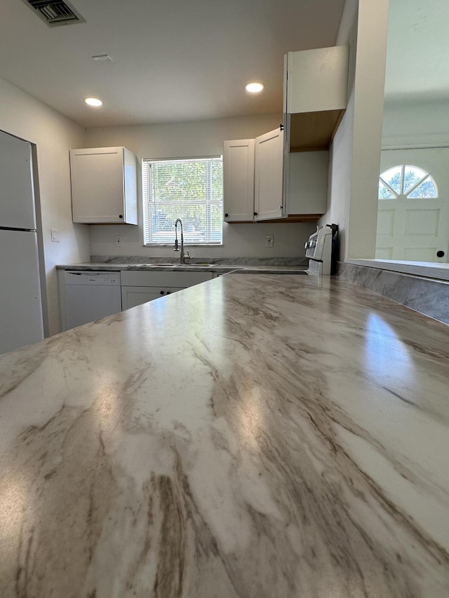 kitchen featuring visible vents, freestanding refrigerator, white cabinets, a sink, and dishwasher