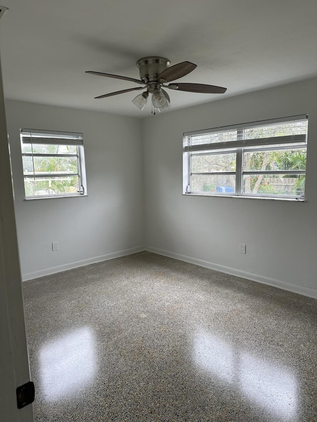 empty room with baseboards, a ceiling fan, and speckled floor