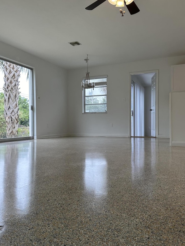 empty room with ceiling fan with notable chandelier, visible vents, a wealth of natural light, and speckled floor