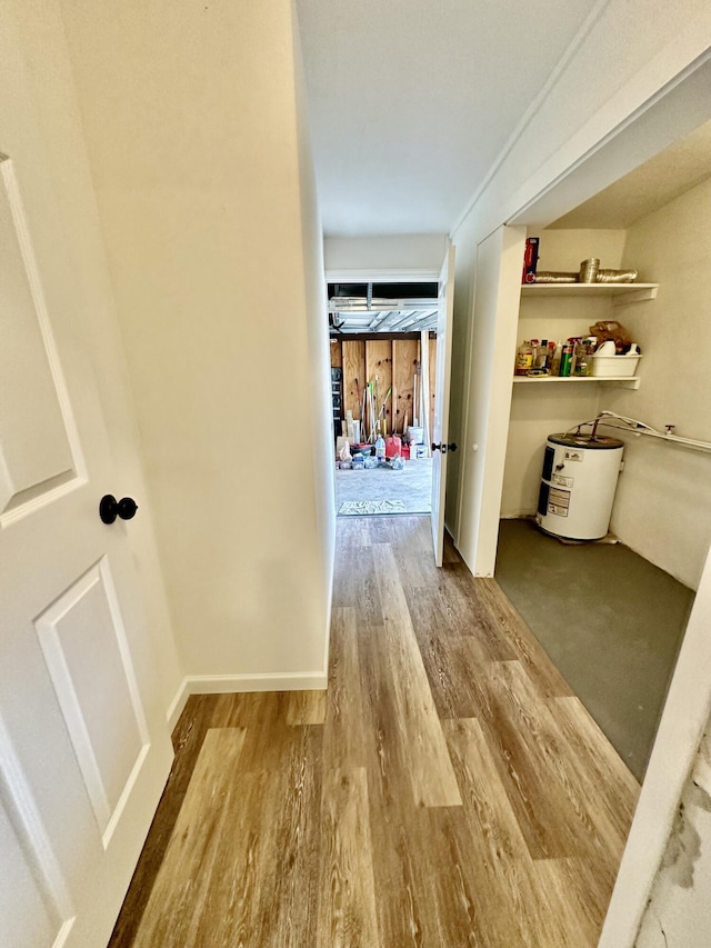 corridor featuring wood finished floors, electric water heater, and baseboards