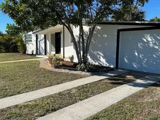 view of front facade with a garage, driveway, a front yard, and stucco siding