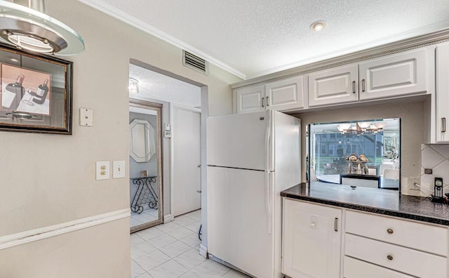 kitchen featuring visible vents, dark countertops, ornamental molding, freestanding refrigerator, and a textured ceiling