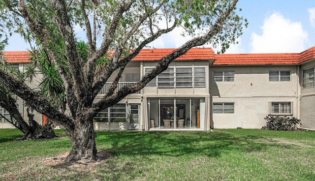 back of house with a yard, a tiled roof, and stucco siding