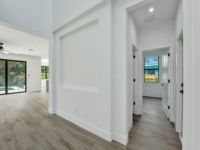 corridor with recessed lighting, visible vents, a towering ceiling, light wood-type flooring, and baseboards