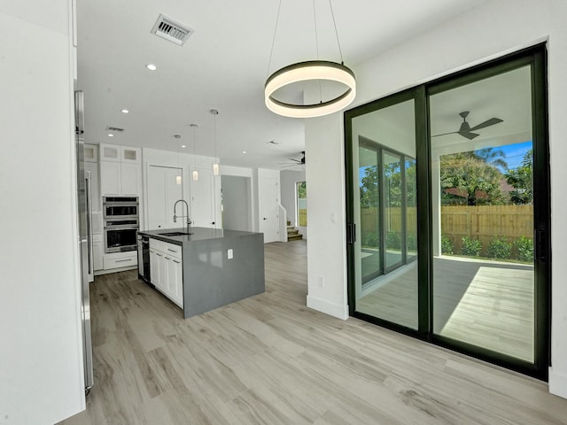 kitchen with decorative light fixtures, dark countertops, visible vents, white cabinetry, and a sink