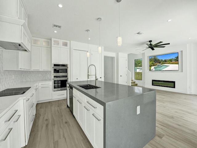 kitchen featuring stainless steel appliances, an island with sink, a sink, and white cabinetry