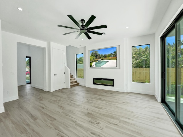 unfurnished living room with baseboards, a glass covered fireplace, light wood-style flooring, stairs, and recessed lighting