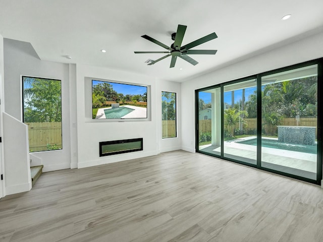 unfurnished living room featuring recessed lighting, light wood-style floors, a glass covered fireplace, a ceiling fan, and baseboards