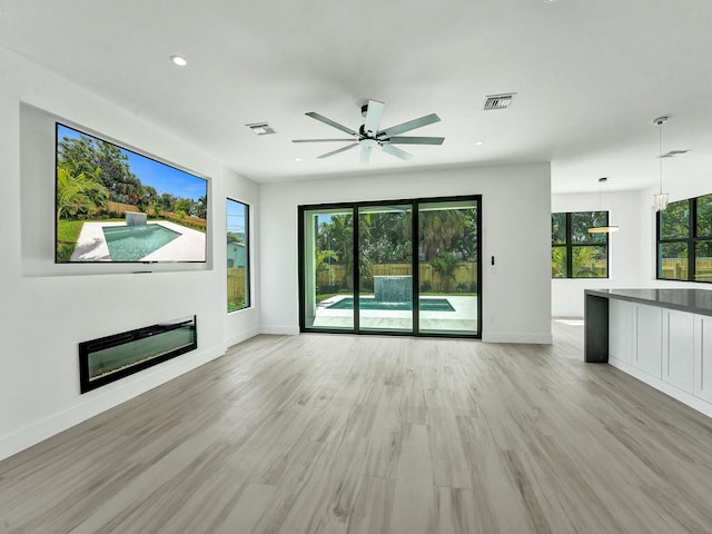 unfurnished living room with light wood finished floors, baseboards, visible vents, a glass covered fireplace, and recessed lighting