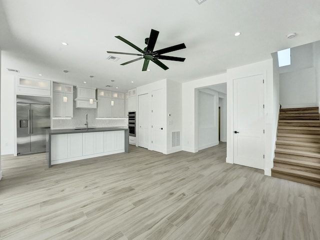 unfurnished living room featuring ceiling fan, a sink, visible vents, stairway, and light wood-type flooring