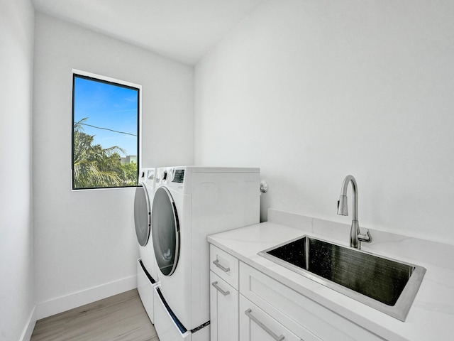 clothes washing area featuring a sink, baseboards, light wood-style floors, independent washer and dryer, and cabinet space