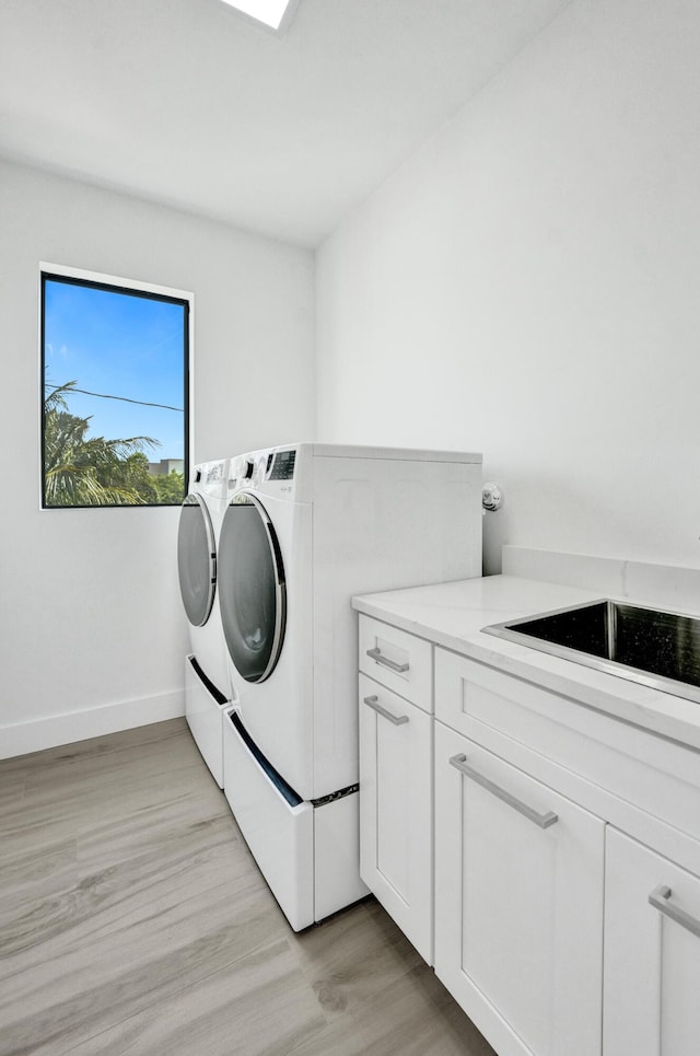 laundry room with light wood finished floors, cabinet space, baseboards, washer and dryer, and a sink