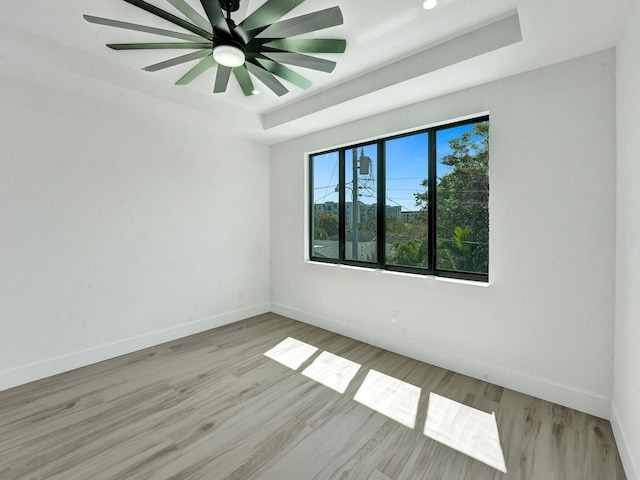 unfurnished room featuring light wood-style floors, baseboards, a tray ceiling, and a ceiling fan