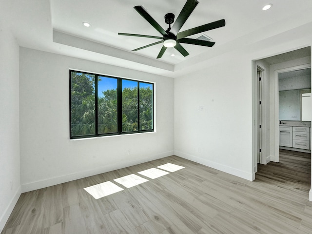 unfurnished bedroom featuring baseboards, a tray ceiling, recessed lighting, and light wood-style floors