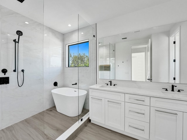 full bath featuring a freestanding bath, double vanity, a sink, and tile walls