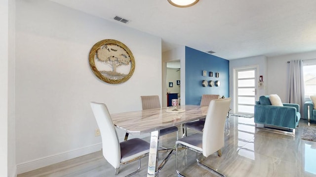 dining room with light wood-type flooring, visible vents, and baseboards