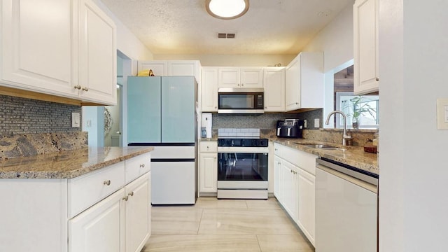 kitchen with white electric stove, white cabinetry, freestanding refrigerator, dishwasher, and stainless steel microwave