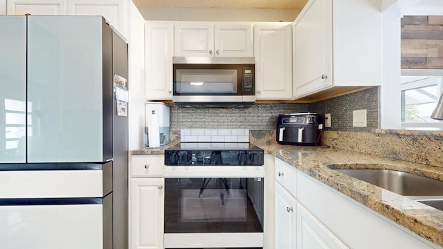 kitchen featuring black electric range, stainless steel microwave, freestanding refrigerator, white cabinetry, and light stone countertops