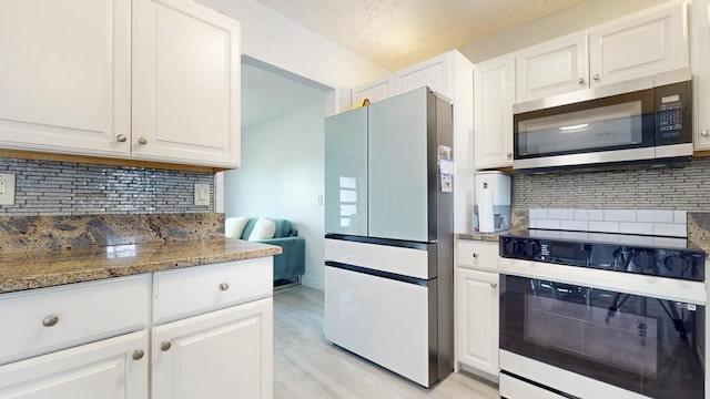 kitchen with backsplash, appliances with stainless steel finishes, white cabinets, and dark stone countertops