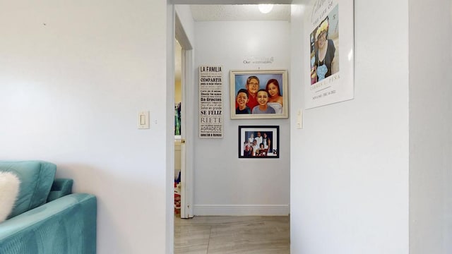 hall with a textured ceiling, light wood-style flooring, and baseboards