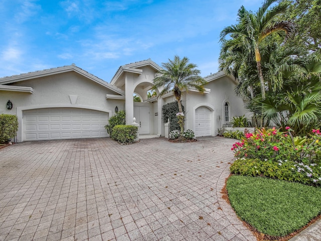 view of front of home with decorative driveway, an attached garage, and stucco siding