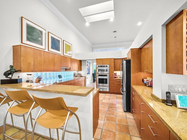 kitchen with a breakfast bar area, stainless steel appliances, a peninsula, a skylight, and brown cabinets