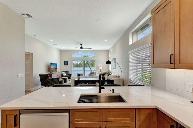 kitchen with visible vents, open floor plan, a sink, light stone countertops, and a peninsula