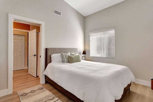 bedroom featuring baseboards, vaulted ceiling, visible vents, and light wood-style floors