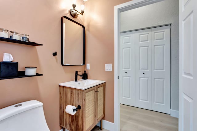 bathroom featuring toilet, wood finished floors, vanity, baseboards, and a closet