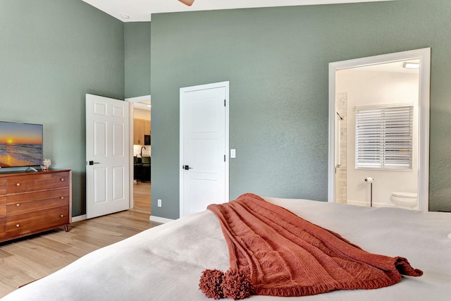 bedroom with light wood-type flooring, ensuite bath, a towering ceiling, and baseboards