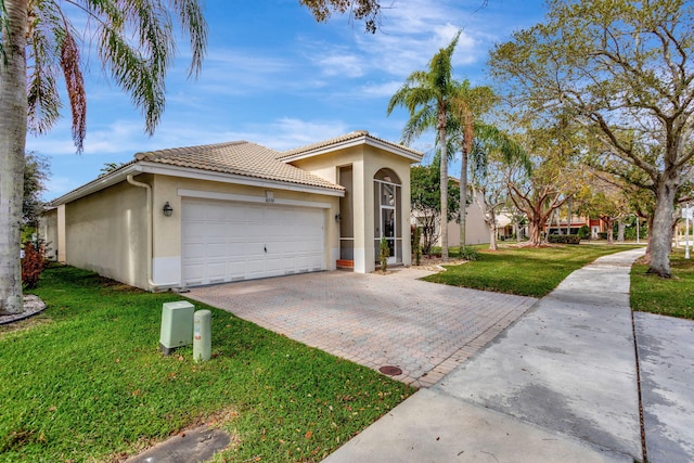 mediterranean / spanish house with a tiled roof, an attached garage, decorative driveway, a front yard, and stucco siding