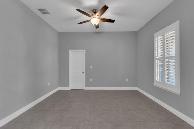 empty room with ceiling fan, light tile patterned floors, visible vents, and baseboards