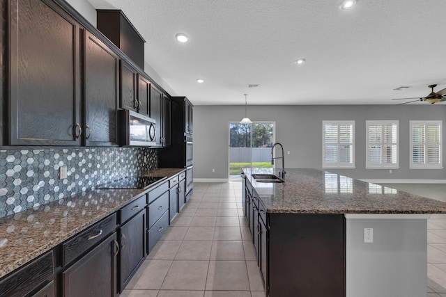 kitchen featuring pendant lighting, a center island with sink, black electric stovetop, stainless steel microwave, and a sink