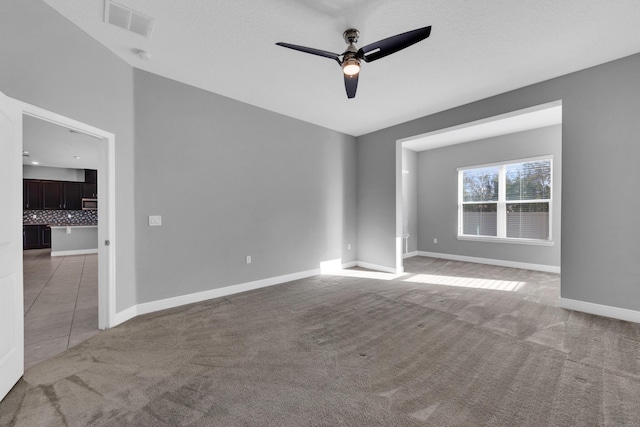 empty room featuring ceiling fan, light tile patterned floors, light carpet, visible vents, and baseboards