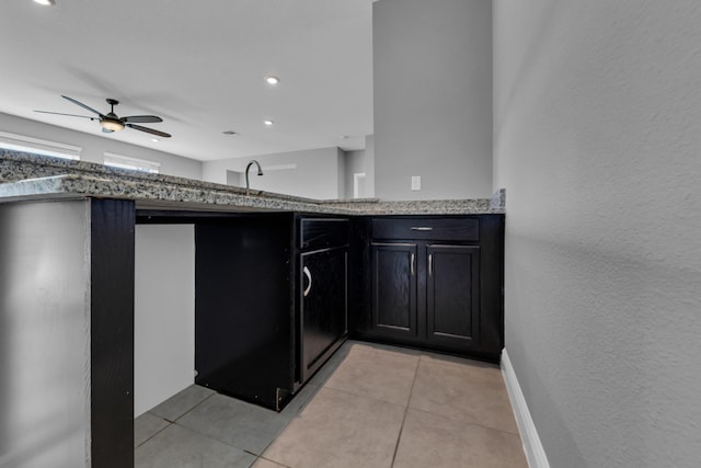 kitchen with light tile patterned floors, stone counters, a ceiling fan, and baseboards