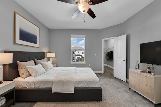 bedroom with light carpet, a walk in closet, a ceiling fan, and baseboards