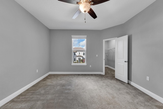 unfurnished bedroom with carpet, a closet, a spacious closet, a ceiling fan, and baseboards