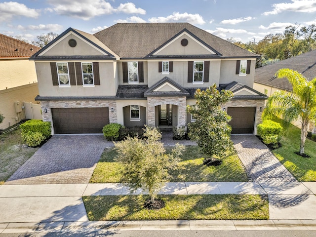 view of front facade featuring decorative driveway, stone siding, an attached garage, and stucco siding