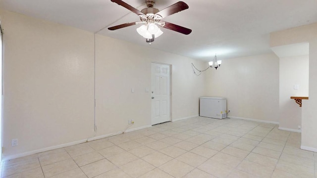 spare room featuring light tile patterned floors, baseboards, and ceiling fan with notable chandelier