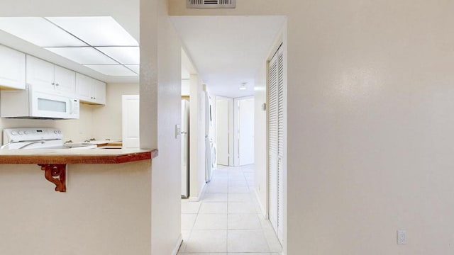 hall featuring visible vents, baseboards, and light tile patterned floors