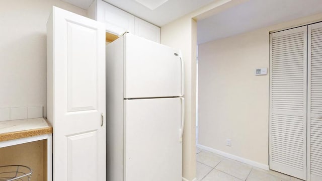 kitchen with light tile patterned floors, baseboards, white cabinets, light countertops, and freestanding refrigerator