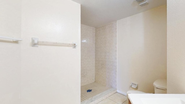 bathroom featuring visible vents, toilet, vanity, tiled shower, and tile patterned floors