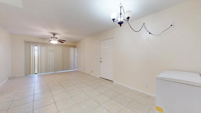 spare room with ceiling fan with notable chandelier, light tile patterned floors, and baseboards